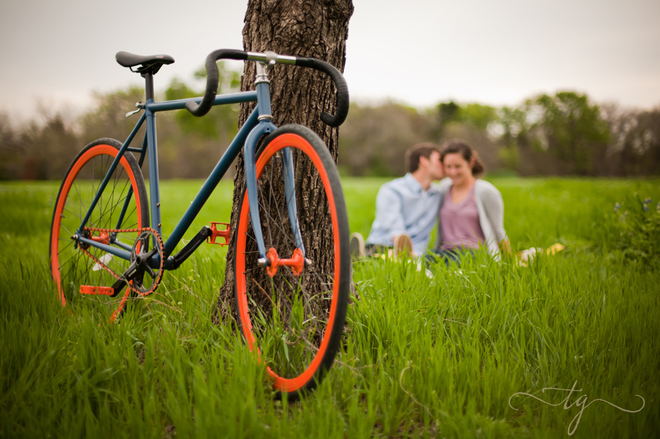 couple sitting together in large green field with bike in foreground