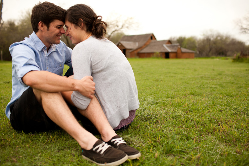 couple snuggling in a field with barn in the distance
